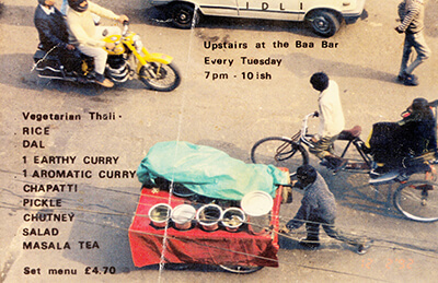 photo from above of Indian street with traffic, pedestrians and a hot food barrow, overlaid with menu and opening times